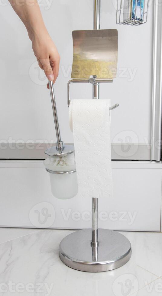 A man takes a toilet brush from a stand. Care and cleanliness of the toilet, close-up. Domestic photo