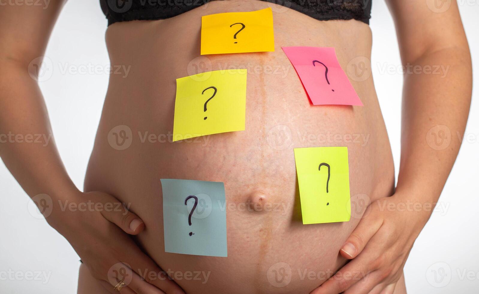 Multi-colored stickers with a question mark are glued on the belly of a pregnant girl. The concept of the uncertainty of the birth of a boy or girl. photo