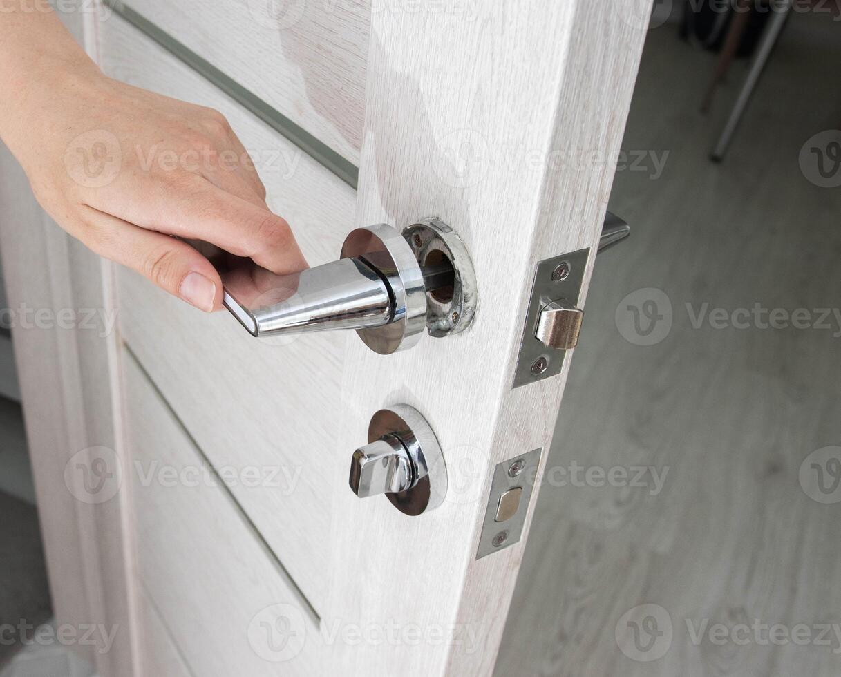 A man's hand opens an interior door with a broken doorknob. Poor quality door hardware, breakage, damage. photo
