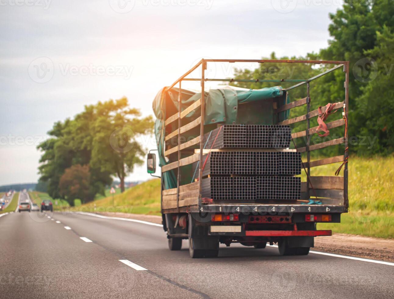 Transportation of metal profiles in a tilt truck on the road in summer, industry. Heavy metal photo