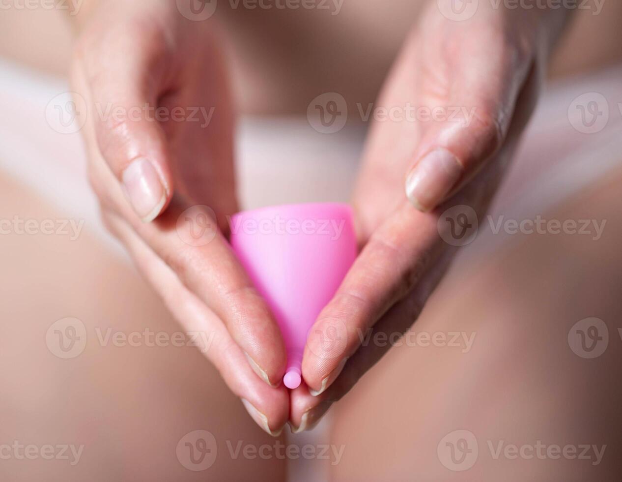 The girl holds in her hands a pink menstrual cup against the background of underwear. Modern silicone medical bowl for collecting discharge during menstruation, close-up photo