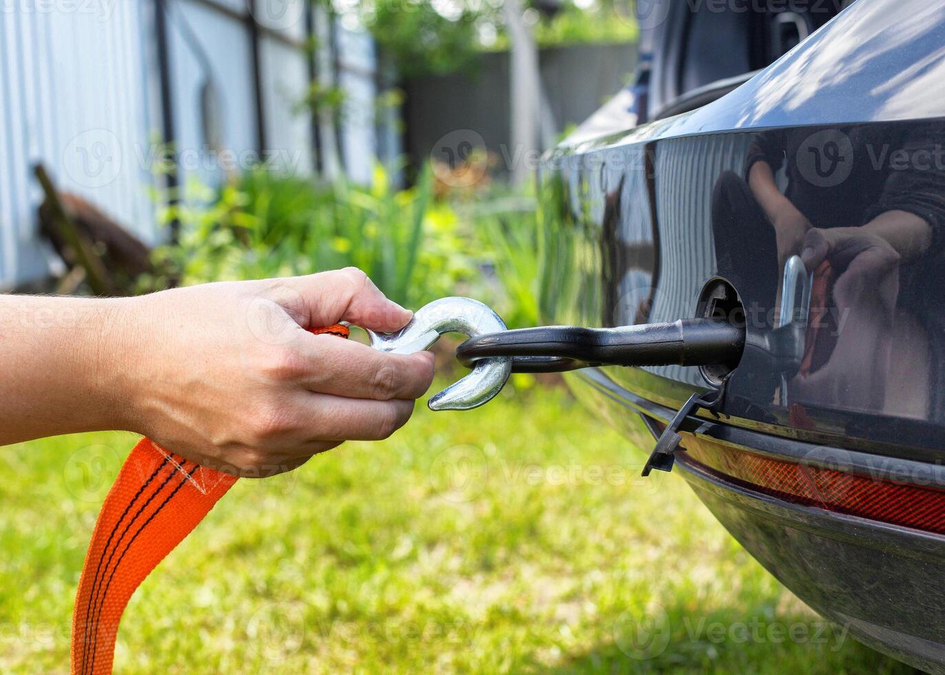 A man's hand clings a tow rope to a tow hook in a passenger car, close-up. Summer photo
