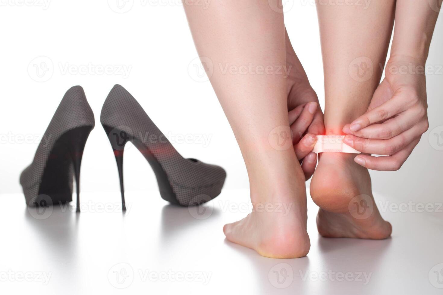 A woman puts a callus plaster on the foot. Nearby lie women's high-heeled shoes photo