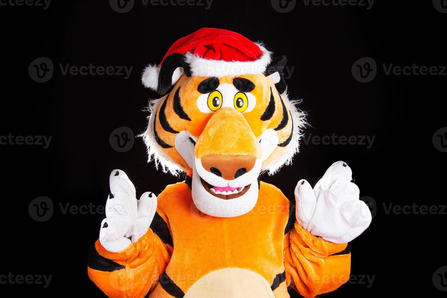 Plush soft orange tiger in a red santa claus hat on a black background. Christmas and new year 2022 concept photo