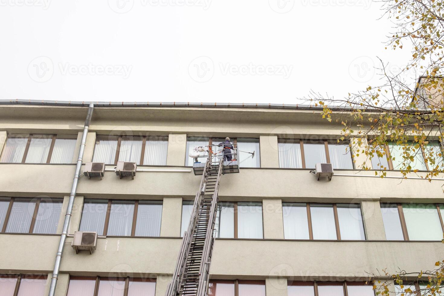 Girl worker washes windows at a height in the house, washer photo