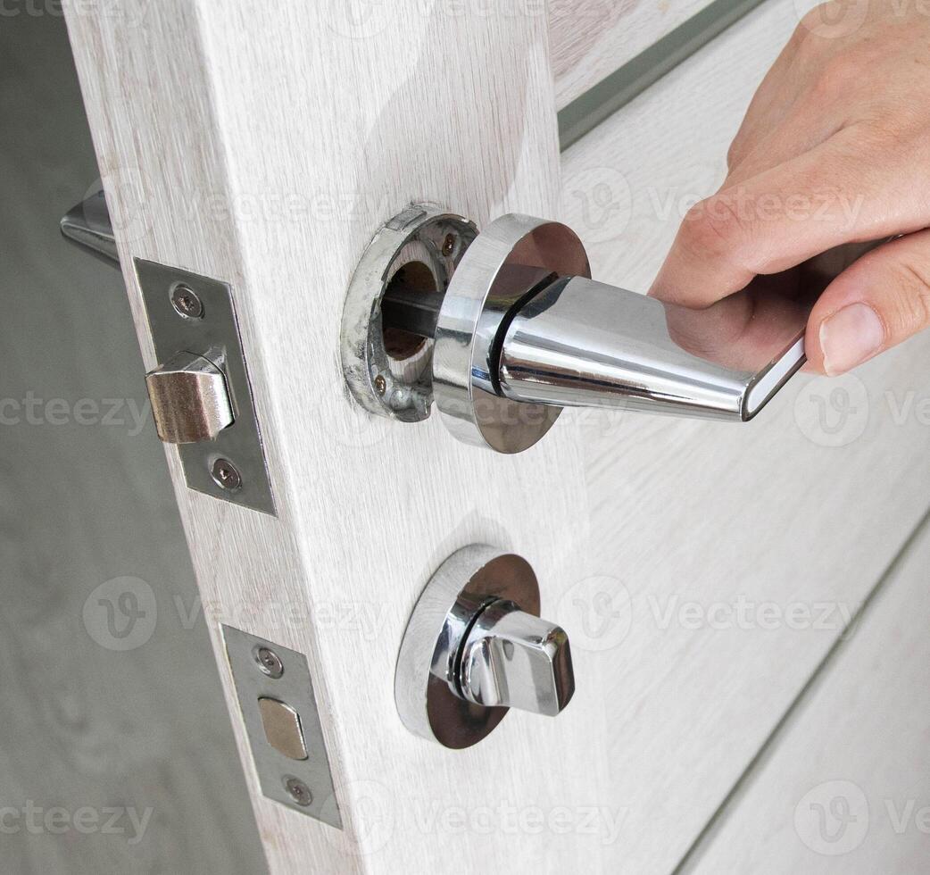 A man's hand opens an interior door with a broken doorknob. Poor quality door hardware, breakage, damage. photo
