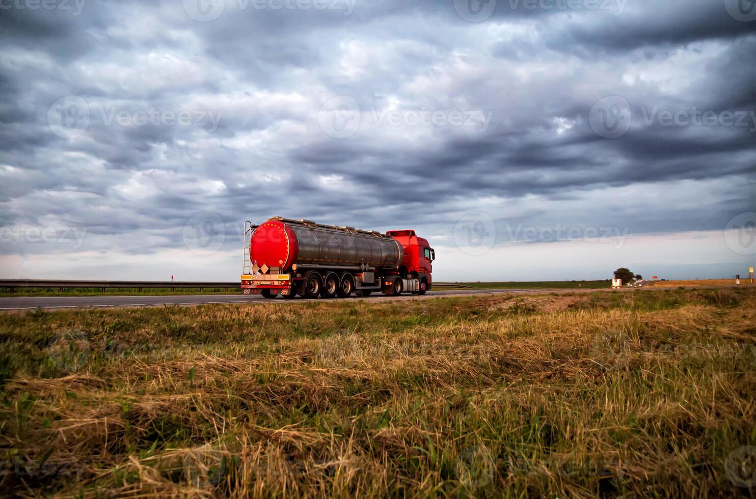 New red truck with a tanker truck transports gasoline against the background of the cloudy sky in the evening. Dangerous goods transport industry photo