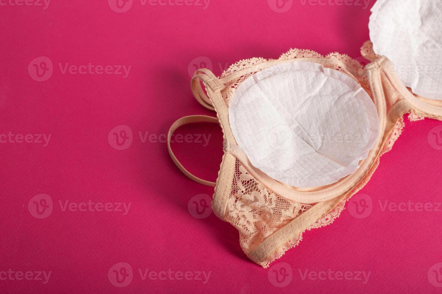 Women's bra with liners against the flow of milk from the breast of a nursing woman on a pink background. Copy space for text photo