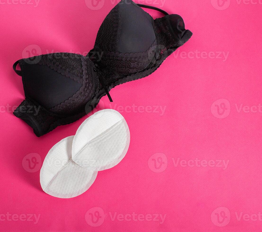 Black bra with liners for the female breast against the flow of milk on a pink background. Womens breast pads, lactation. Copy space for text photo