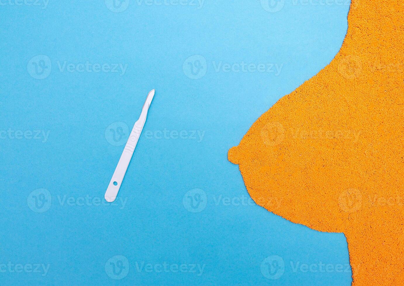 Medical scalpel on a blue background with female breast from plasticine. The concept of augmentation or reduction of the garlic breast with plastic surgery photo