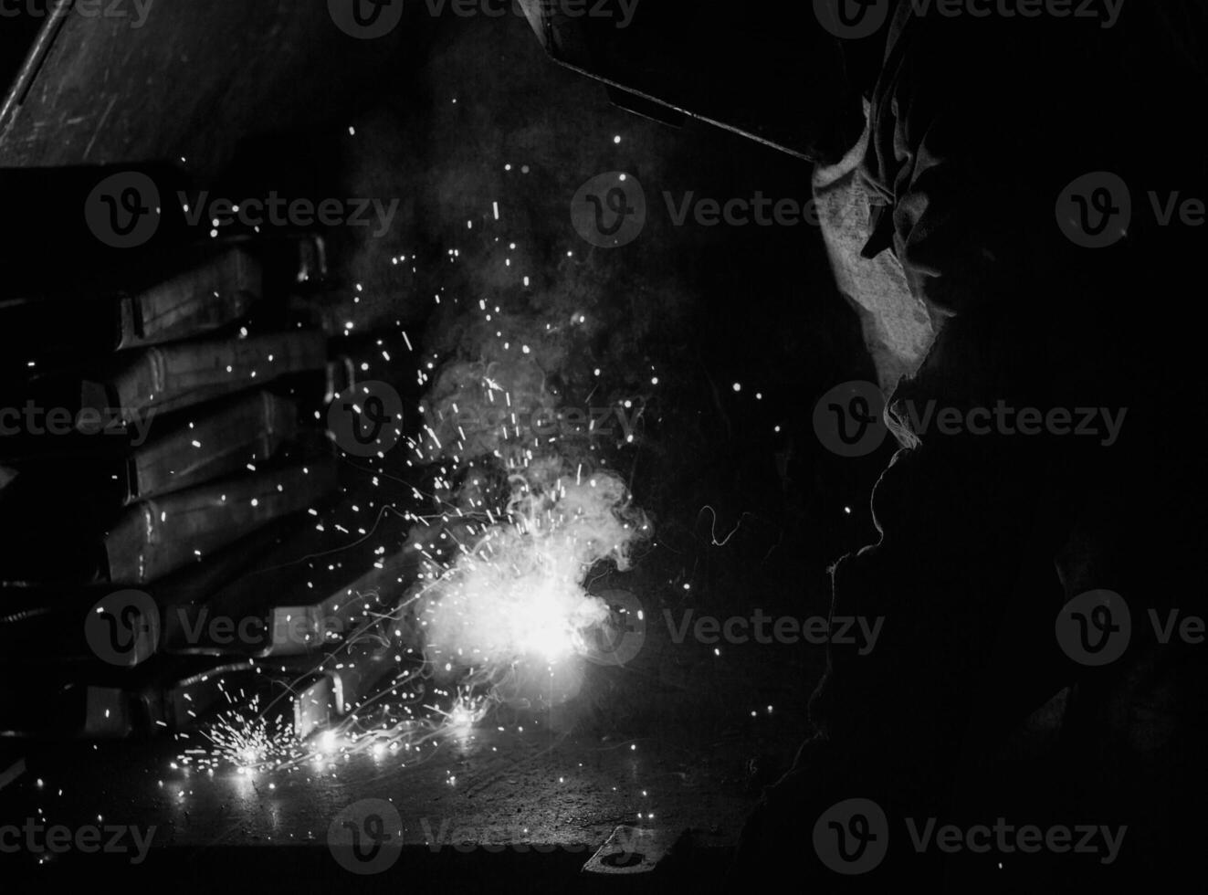 Welder at the factory in a welding mask welds metal parts, welding and sparks, black and white, worker photo