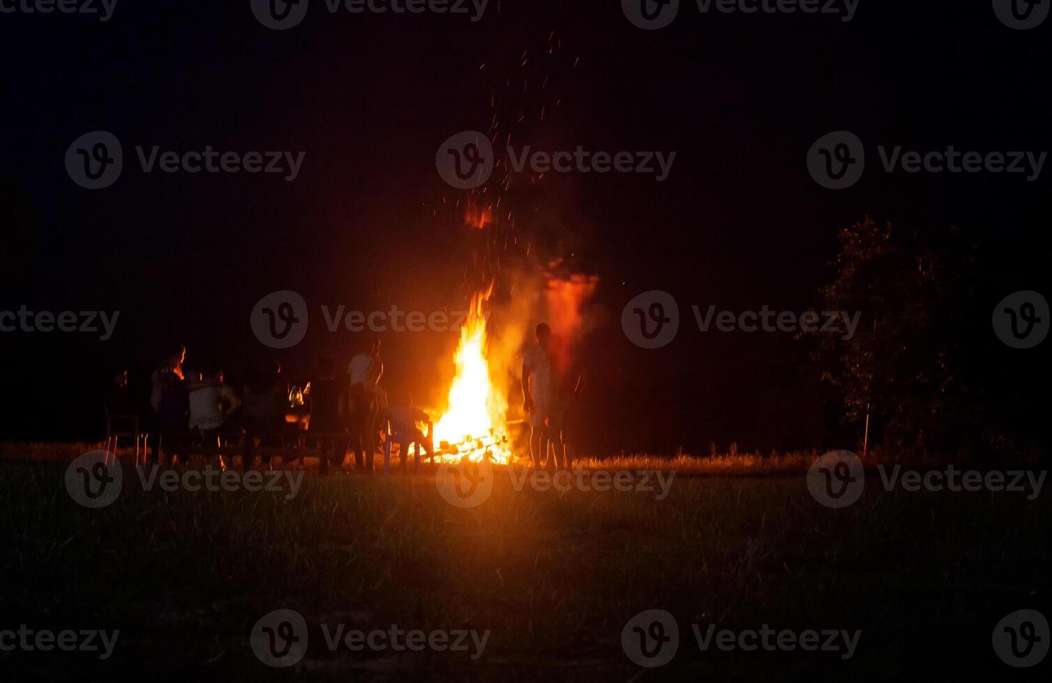 People relax on a holiday in the forest near a large bonfire at night. National holiday background, copy space photo