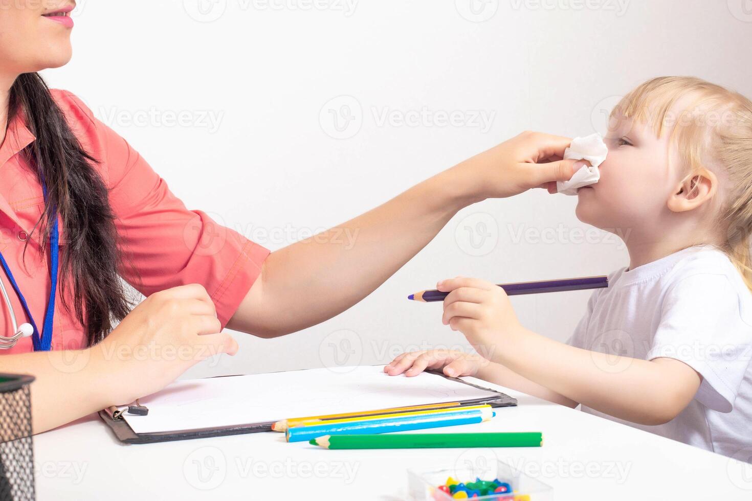Doctor pediatrician wipes the nose from snot to a child a little girl 3 years old. The concept of treating a runny nose in children and nasal congestion. Bacterial infection, copy space photo