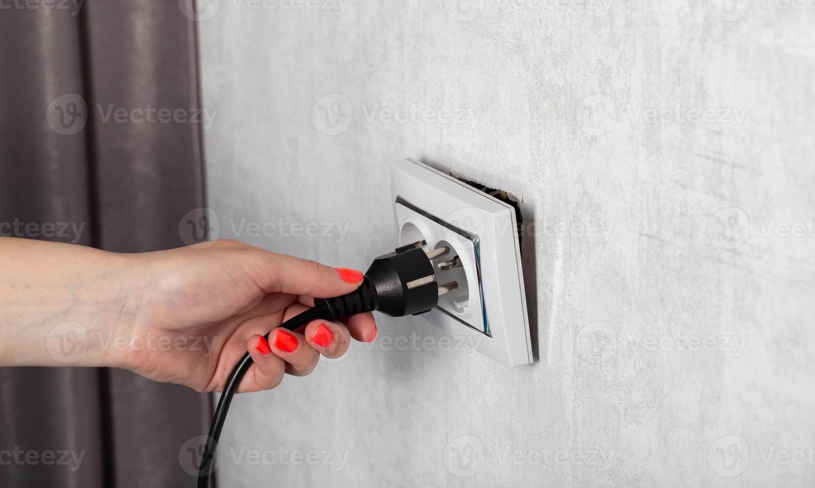 The girl removes the electrical plug from the socket and breaks the socket out of the socket. Incorrect removal of the electrical plug. Risk of electric shock, close-up photo