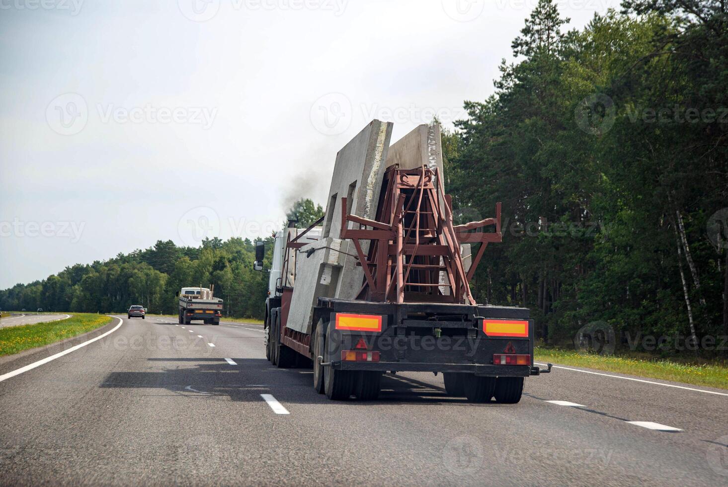 Semi-trailer truck tractor panel transporter transports reinforced concrete slabs for building a house. Transportation of spare parts for the house on the background of the forest on the highway. photo
