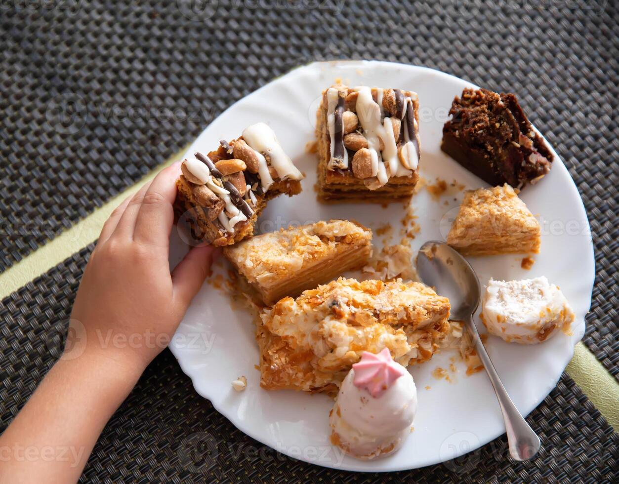 Child's hand holds a cake in a plate, scraps of sweets. Sweet tooth, close-up photo