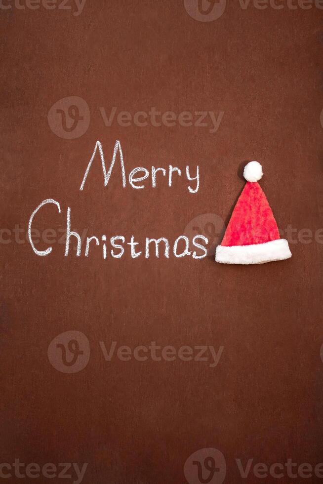 Merry Christmas handwritten in chalk, with Santa's hat nearby, on an abstract background. With space for text photo