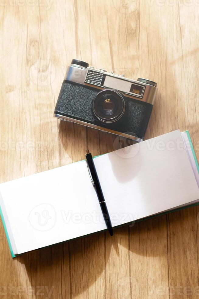 A retro film camera and a notepad with a pen lie on a wooden table, under the rays of the morning sun photo