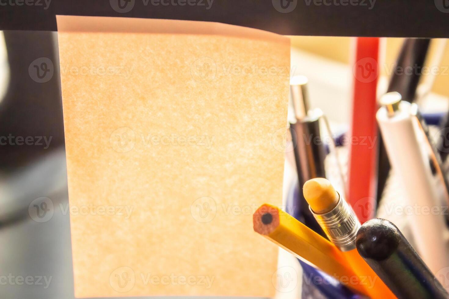 There is a blank sticker for text hanging on the monitor, and pens and pencils are lying nearby, a background for an office-themed inscription photo