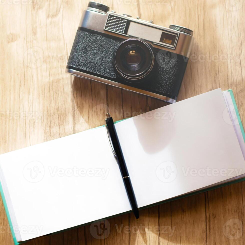 A retro film camera and a notepad with a pen lie on a wooden table, under the rays of the morning sun photo