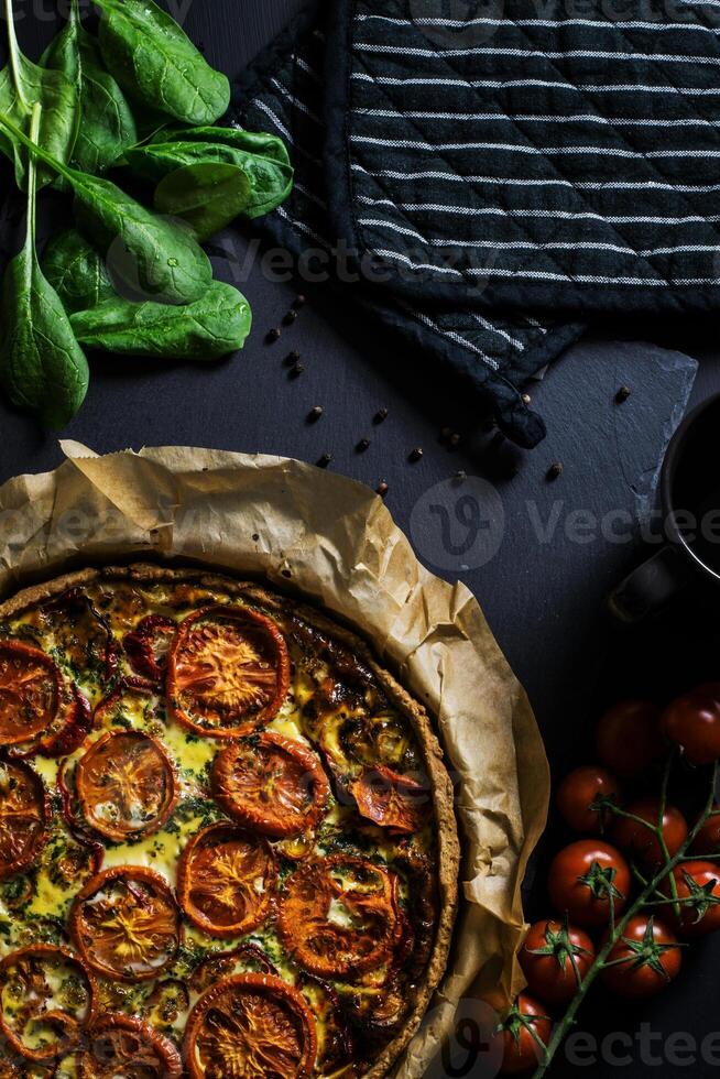 a pizza with tomatoes and spinach on a black background photo