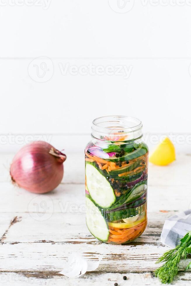 a jar filled with vegetables and herbs sits on a table photo