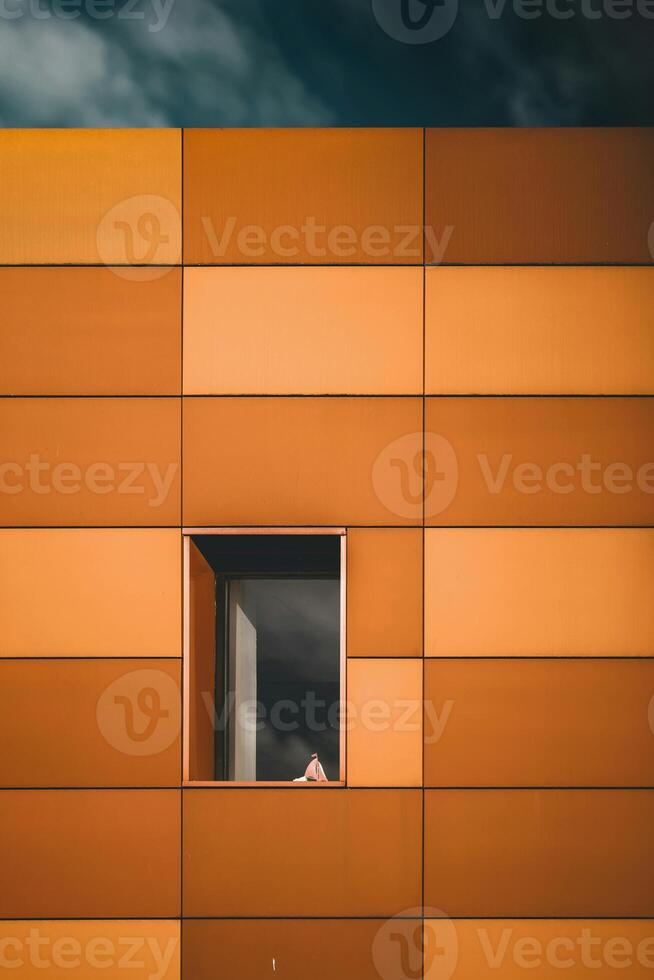 a person looking out of a window of an orange building photo
