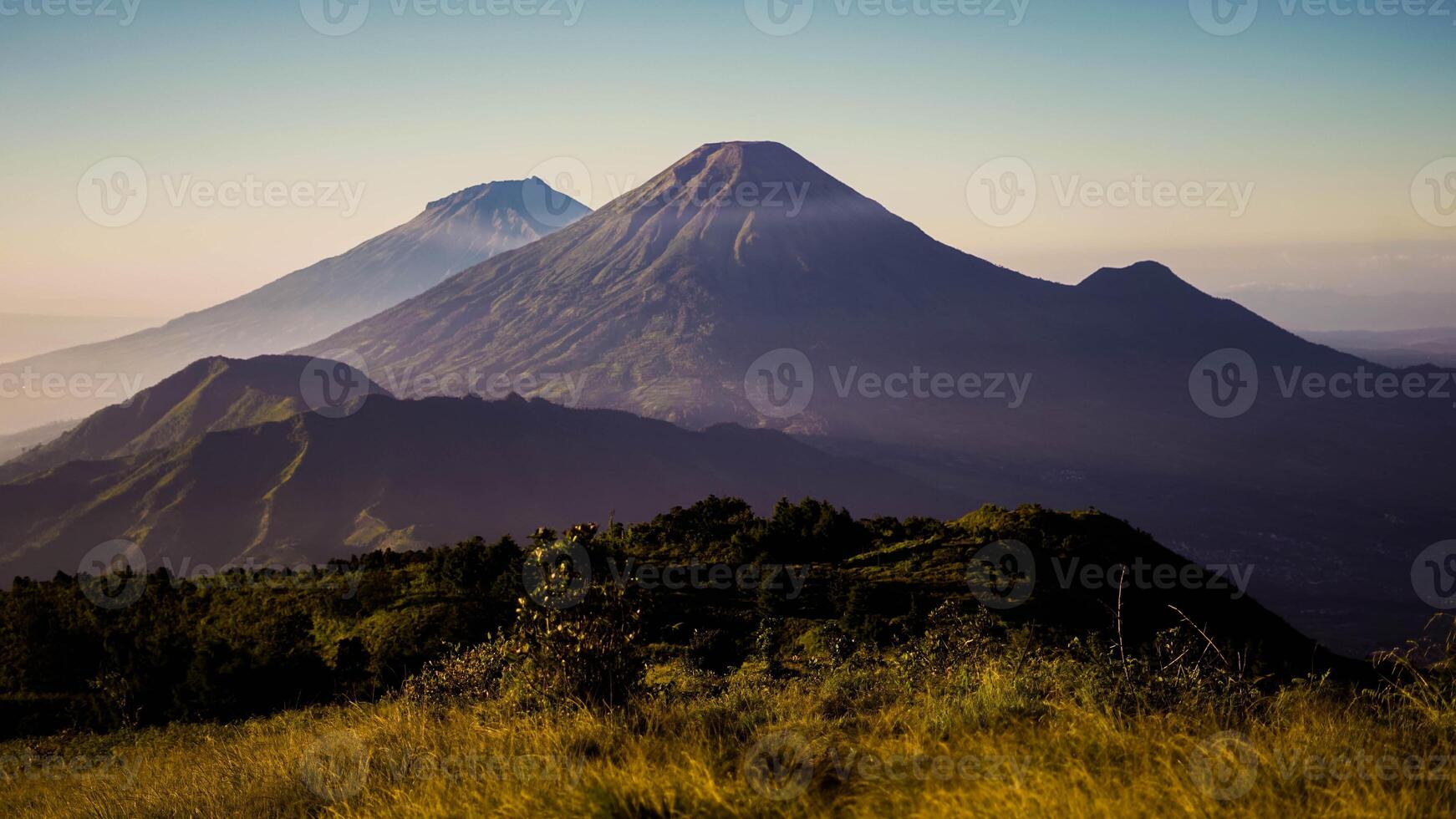 From the summit of Mount Prau, breathtaking views of three towering peaks unfold. A favorite among hikers, this stunning landscape showcases Indonesia's natural beauty and adventure. photo