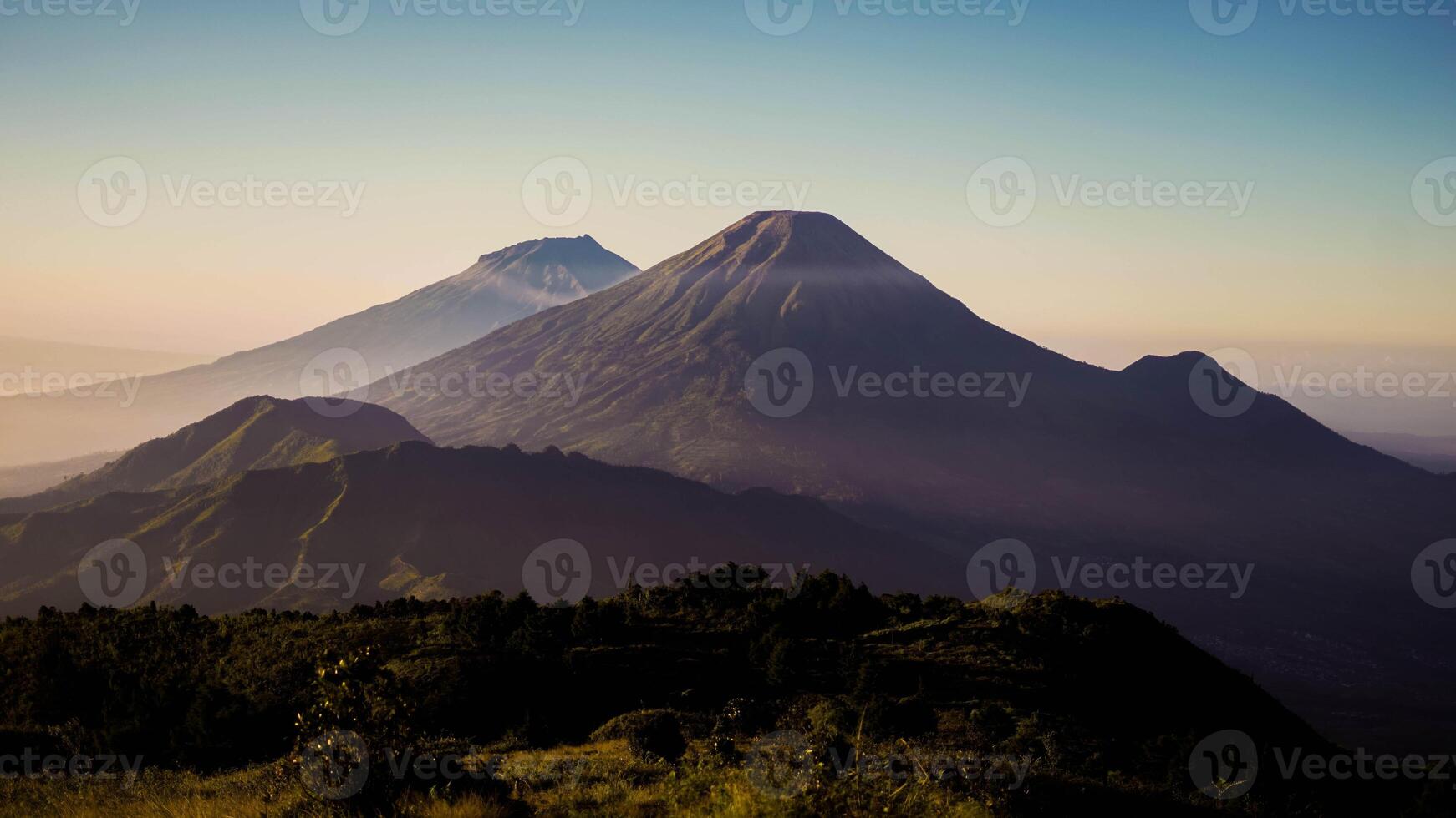 From the summit of Mount Prau, breathtaking views of three towering peaks unfold. A favorite among hikers, this stunning landscape showcases Indonesia's natural beauty and adventure. photo