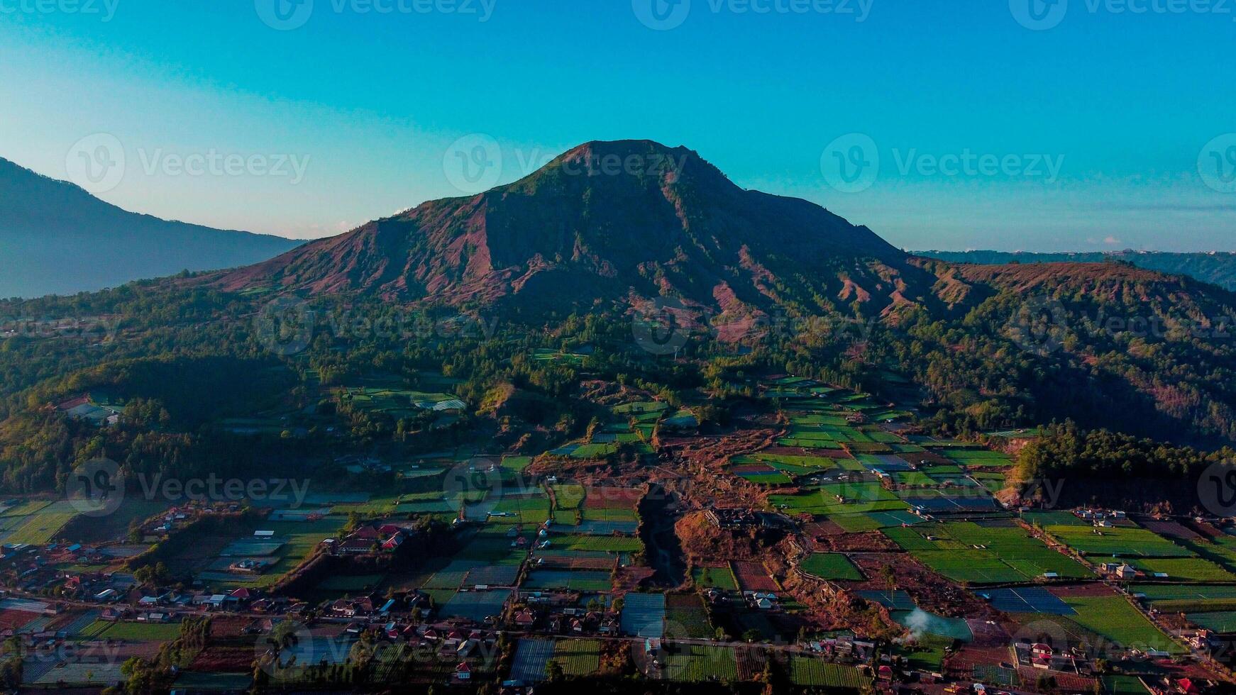 A stunning sunrise over Mount Batur and Mount Agung in Bali reveals mist-covered settlements and lush green plantations. photo