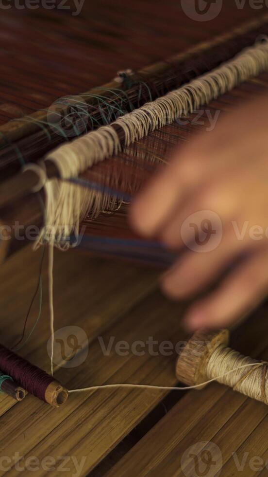 A Baduy woman weaves in front of her home using traditional tools. Her skilled hands create beautiful patterns, preserving cultural heritage and artistry. photo