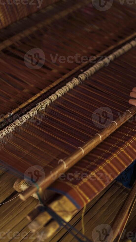 A Baduy woman weaves in front of her home using traditional tools. Her skilled hands create beautiful patterns, preserving cultural heritage and artistry. photo