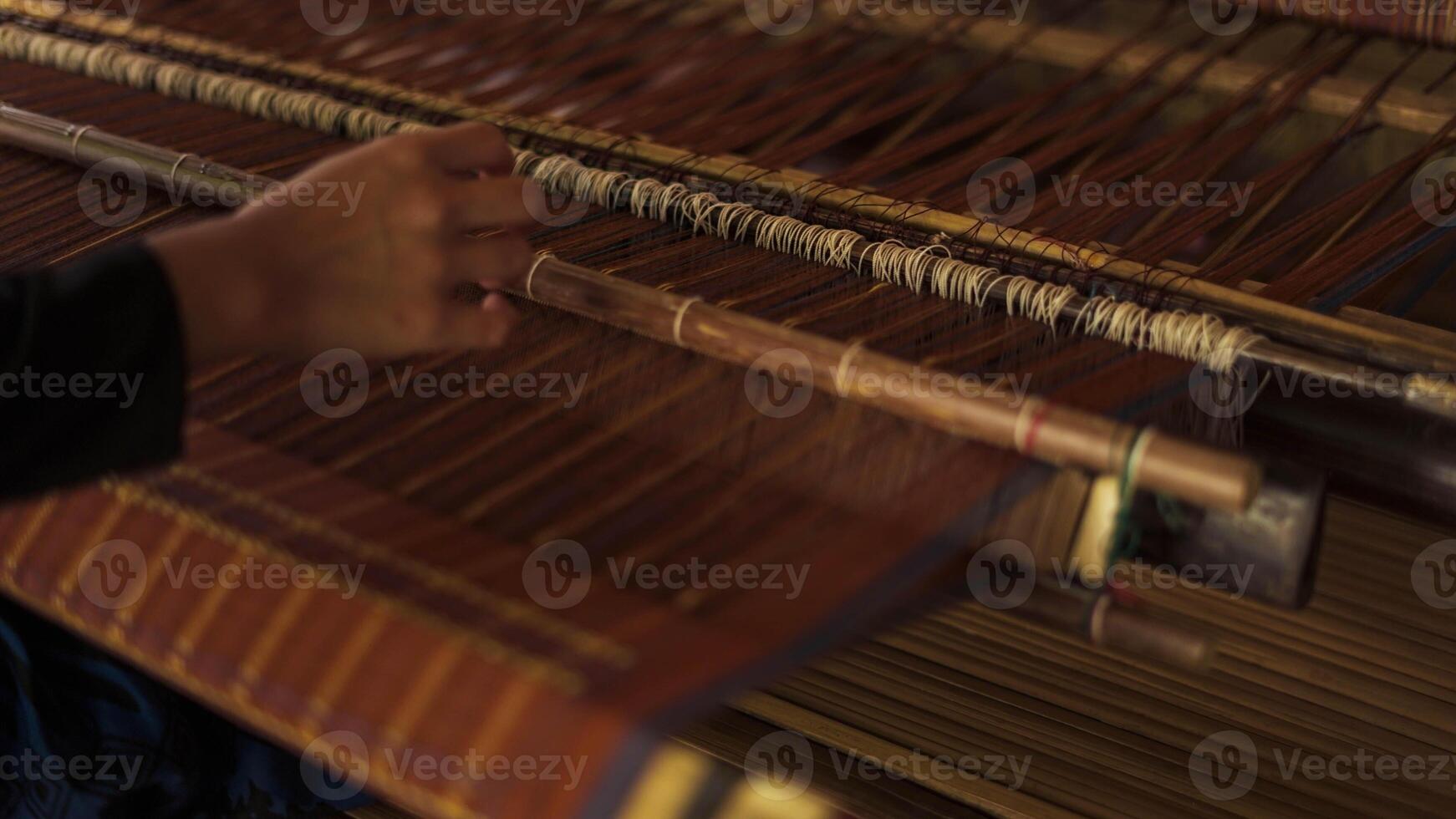 A Baduy woman weaves in front of her home using traditional tools. Her skilled hands create beautiful patterns, preserving cultural heritage and artistry. photo