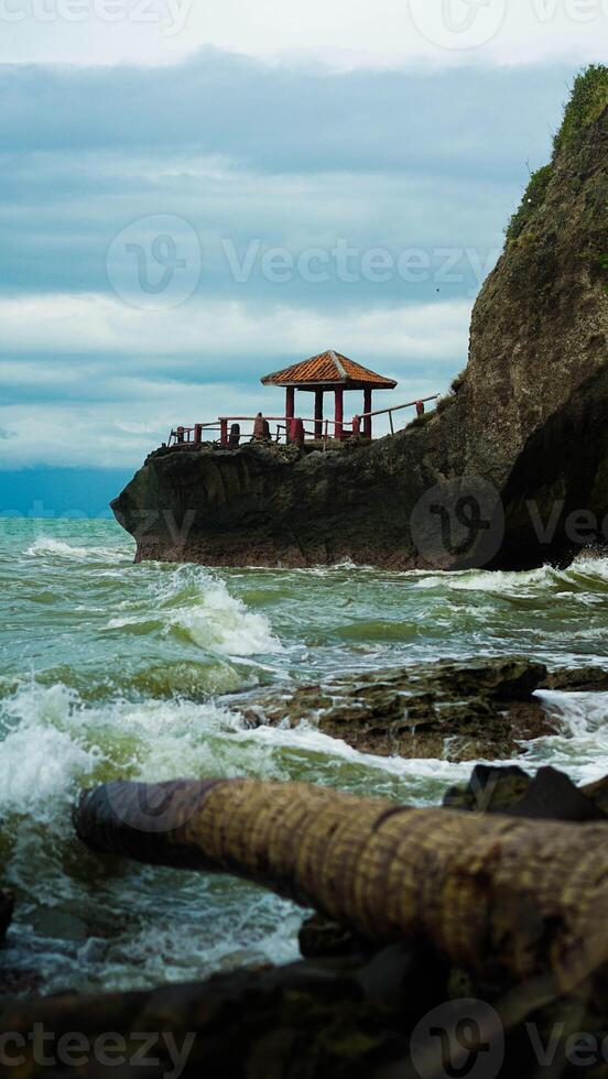 A beautiful beach in Banten, Indonesia, sits atop cliffs with crashing waves. A cozy resting spot offers a perfect view of the stunning shoreline. photo