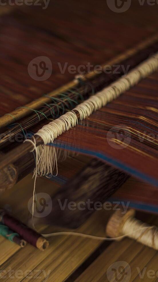 A Baduy woman weaves in front of her home using traditional tools. Her skilled hands create beautiful patterns, preserving cultural heritage and artistry. photo