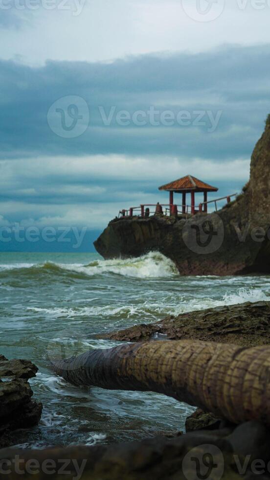 A beautiful beach in Banten, Indonesia, sits atop cliffs with crashing waves. A cozy resting spot offers a perfect view of the stunning shoreline. photo