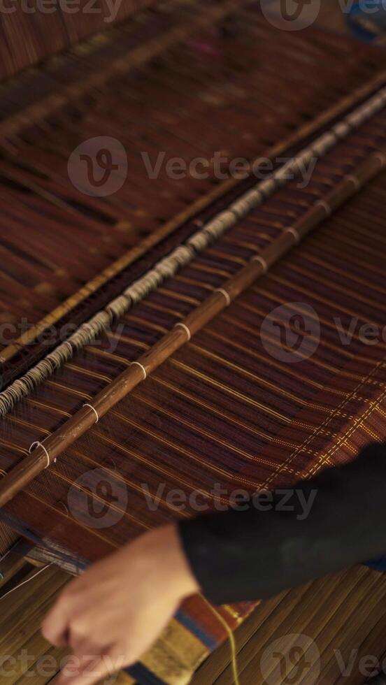 A Baduy woman weaves in front of her home using traditional tools. Her skilled hands create beautiful patterns, preserving cultural heritage and artistry. photo