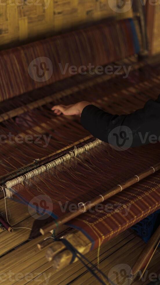 A Baduy woman weaves in front of her home using traditional tools. Her skilled hands create beautiful patterns, preserving cultural heritage and artistry. photo
