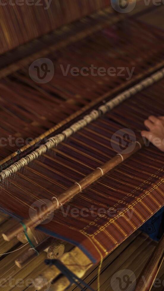 A Baduy woman weaves in front of her home using traditional tools. Her skilled hands create beautiful patterns, preserving cultural heritage and artistry. photo