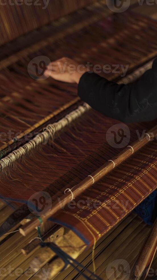 A Baduy woman weaves in front of her home using traditional tools. Her skilled hands create beautiful patterns, preserving cultural heritage and artistry. photo