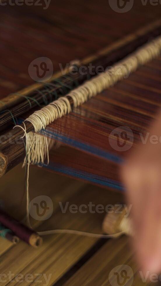 A Baduy woman weaves in front of her home using traditional tools. Her skilled hands create beautiful patterns, preserving cultural heritage and artistry. photo
