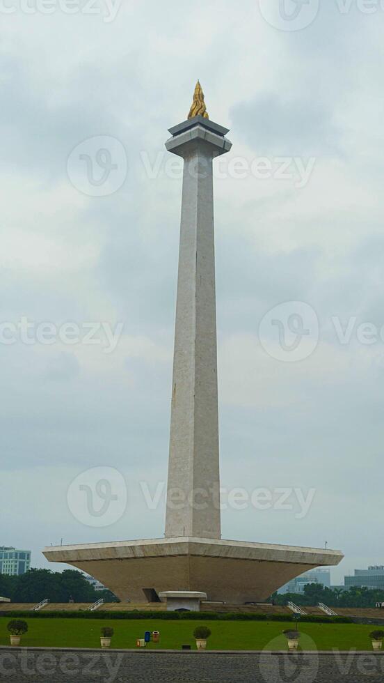 The iconic Monas in Jakarta stands tall against a backdrop of beautiful clouds and lush green grass photo