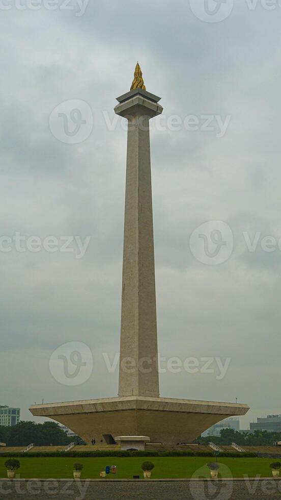 The iconic Monas in Jakarta stands tall against a backdrop of beautiful clouds and lush green grass photo