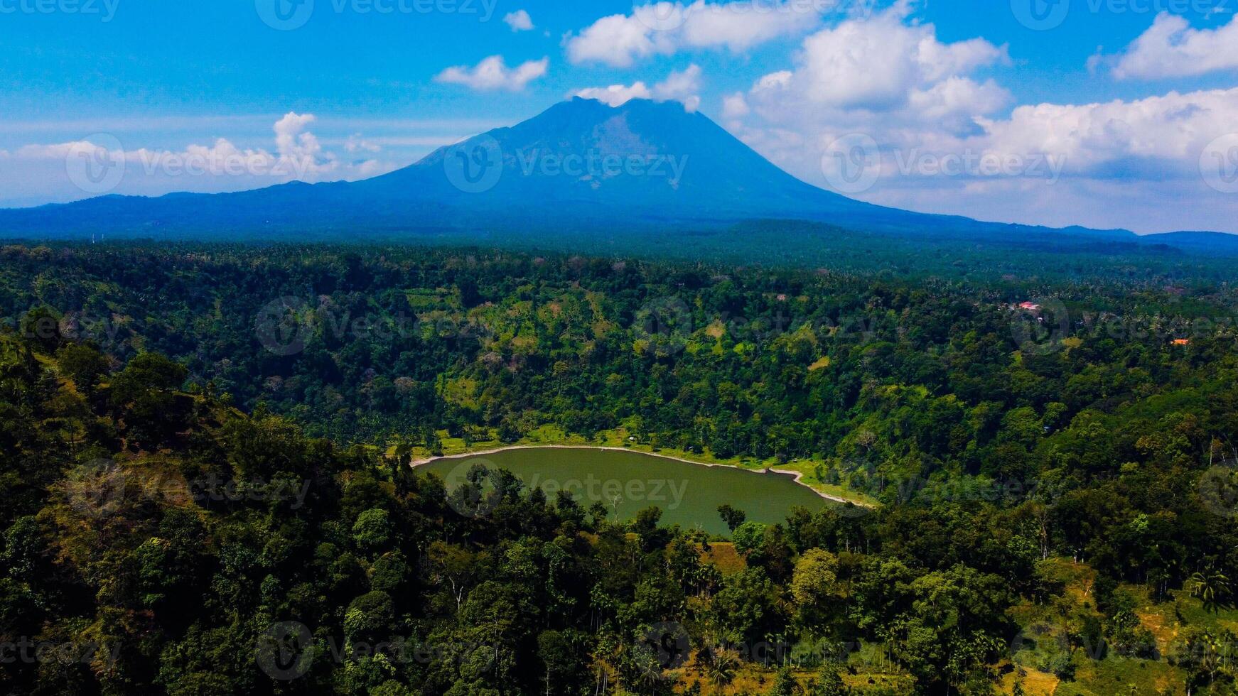 Ranu Bedali Lake in East Java sparkles under a clear blue sky, with Mount Semeru majestically rising in the background. The stunning clouds add to the serene beauty of this breathtaking landscape. photo