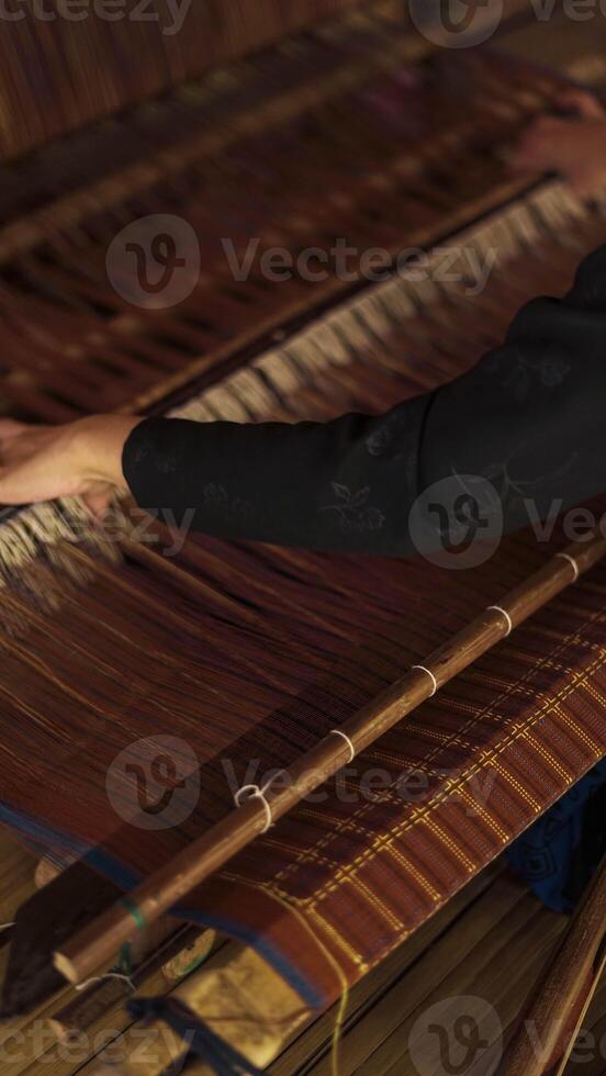 A Baduy woman weaves in front of her home using traditional tools. Her skilled hands create beautiful patterns, preserving cultural heritage and artistry. photo