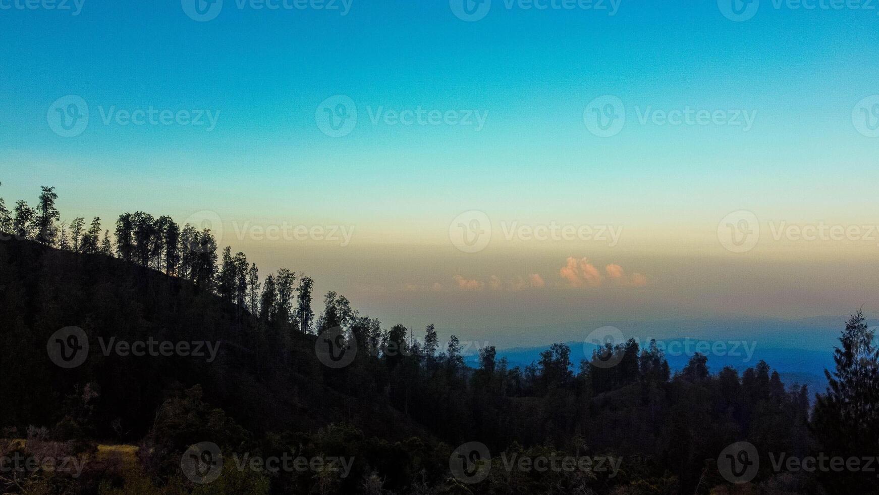 An aerial view of Mount Tambora's peak reveals a breathtaking landscape under a blue sky, as the sun rises, casting golden hues over the stunning terrain. photo