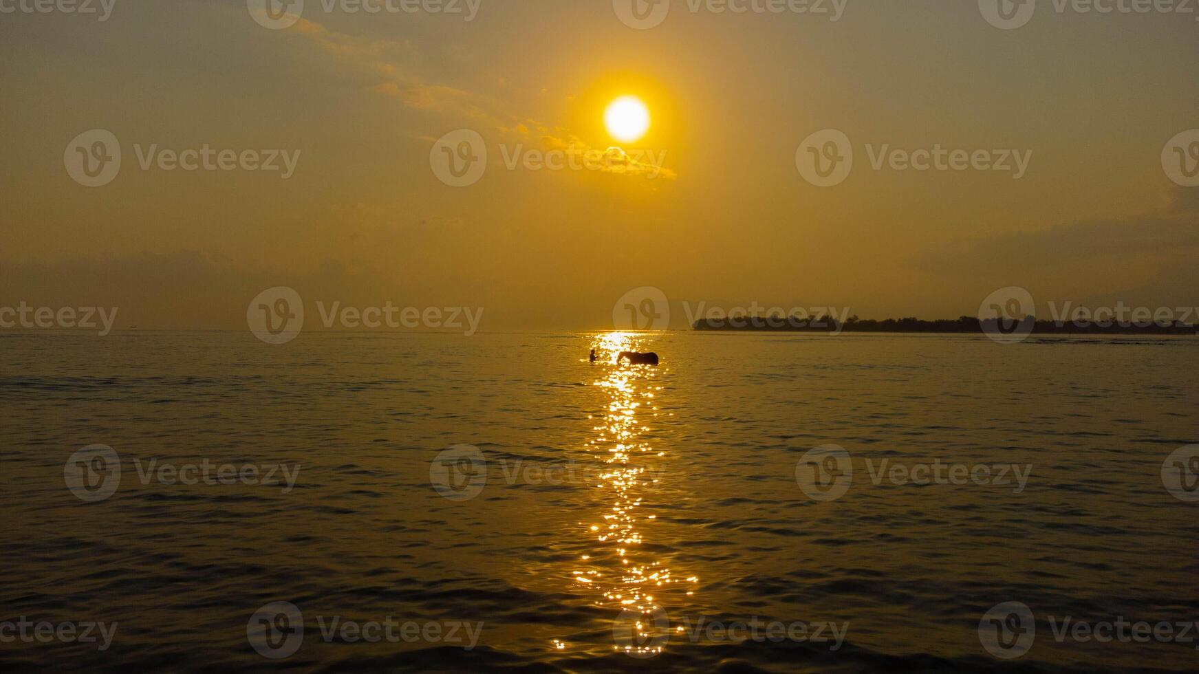 The sunrise casts a golden glow over Gili Trawangan, as the sun rises from the clear blue ocean. The breathtaking beauty creates a perfect tropical morning. photo