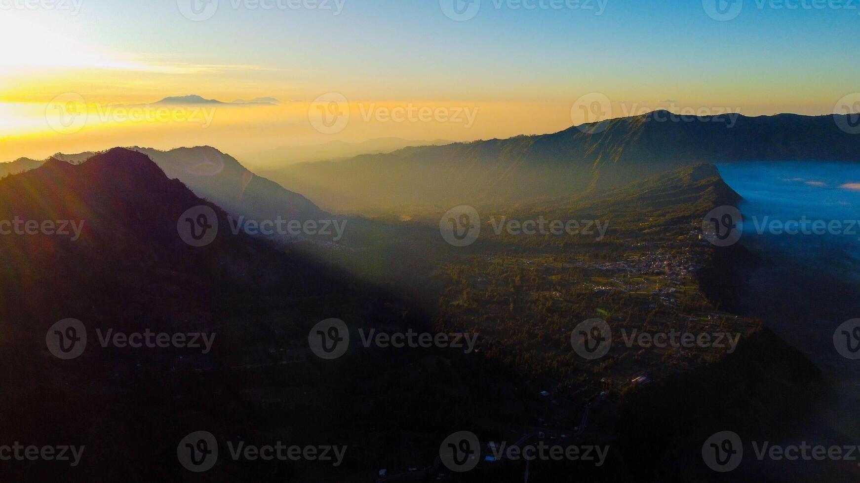 A stunning sunrise at Mount Bromo reveals a vibrant sunset, with clouds gracefully enveloping the peak, showcasing East Java's natural beauty. photo