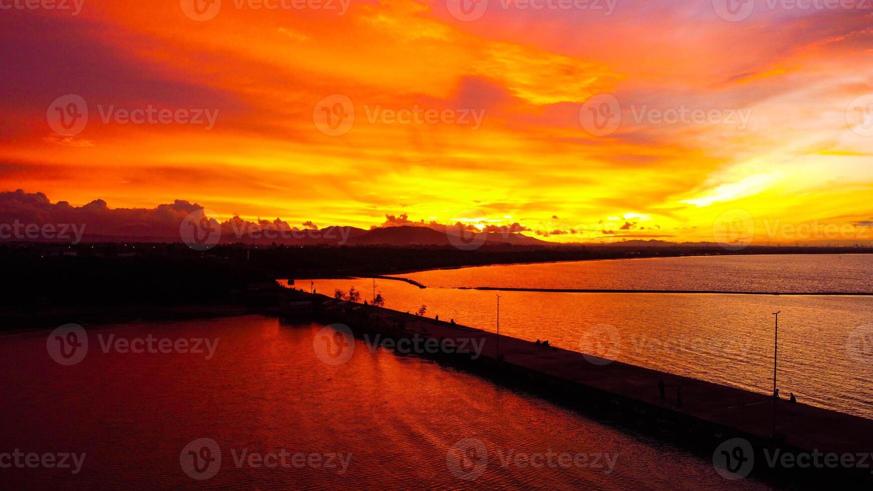 A stunning sunset in Indonesia paints the sky in vibrant oranges and reds. People gather, savoring the breathtaking view and the tranquility it brings. photo