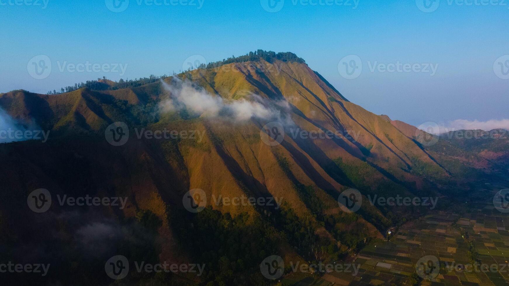 Experience breathtaking aerial views of the rolling hills in Sembalun, at the foot of Mount Rinjani, with expansive savanna turning golden at sunrise. photo
